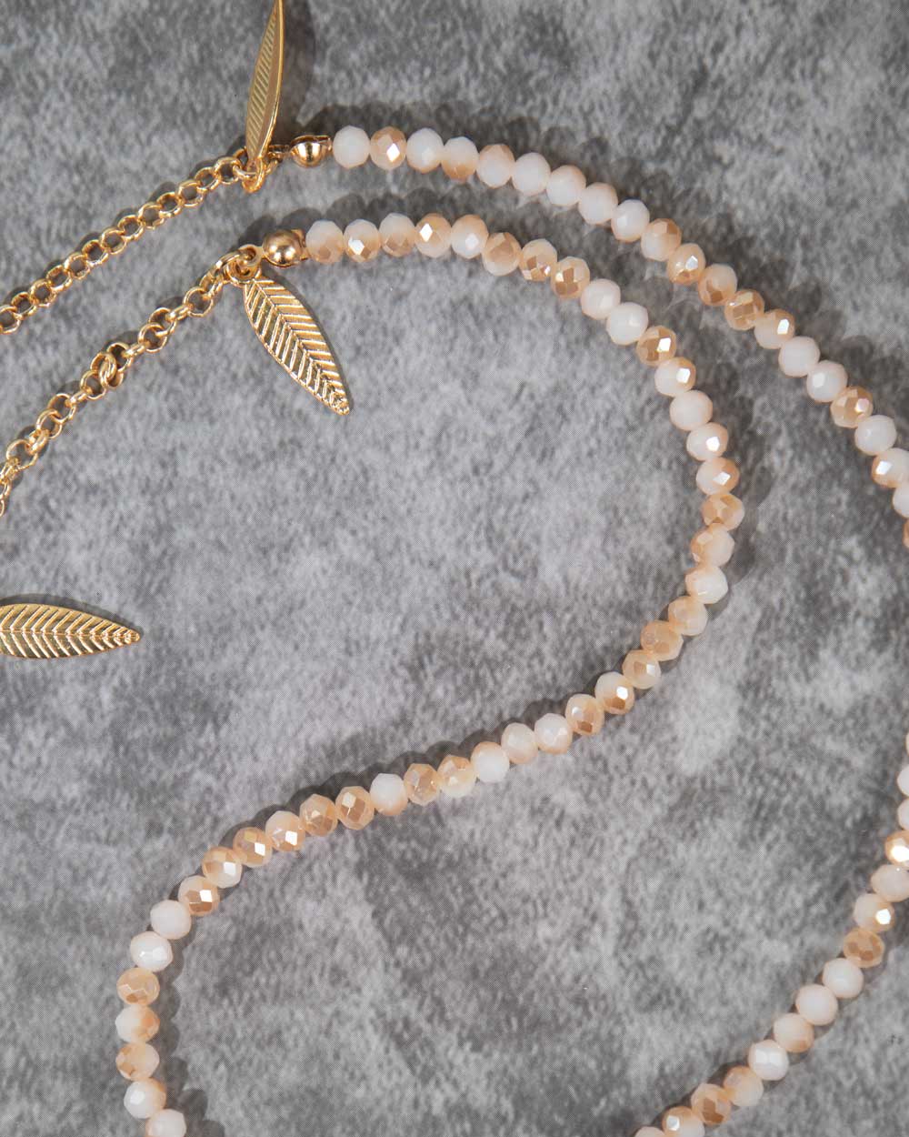 Brillenkoord met gouden veertjes en kraaltjes op een grijze achtergrond.